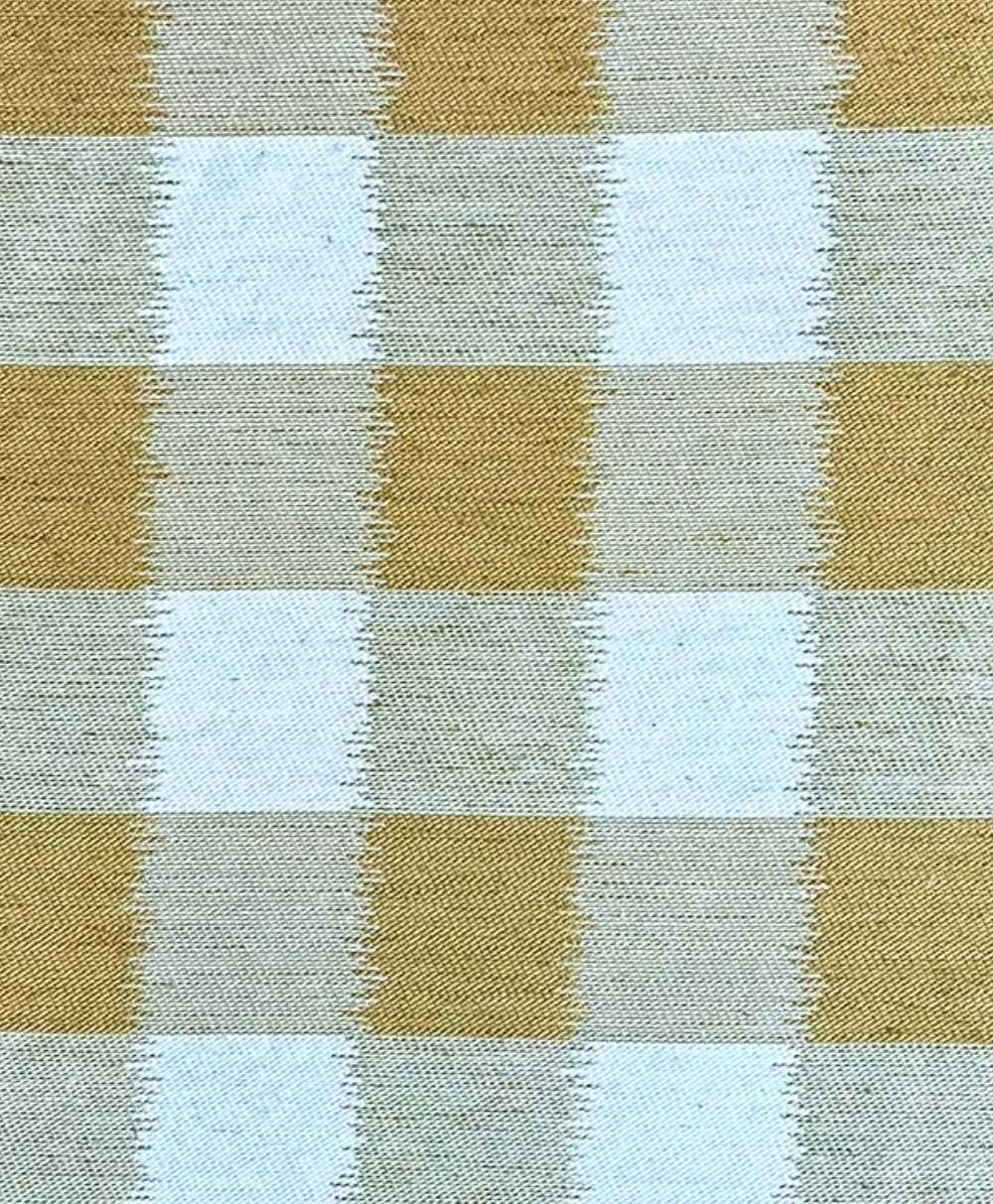A close-up of a textured fabric with a checkered pattern in alternating light blue and tan squares, each outlined with subtle zigzag stitching.