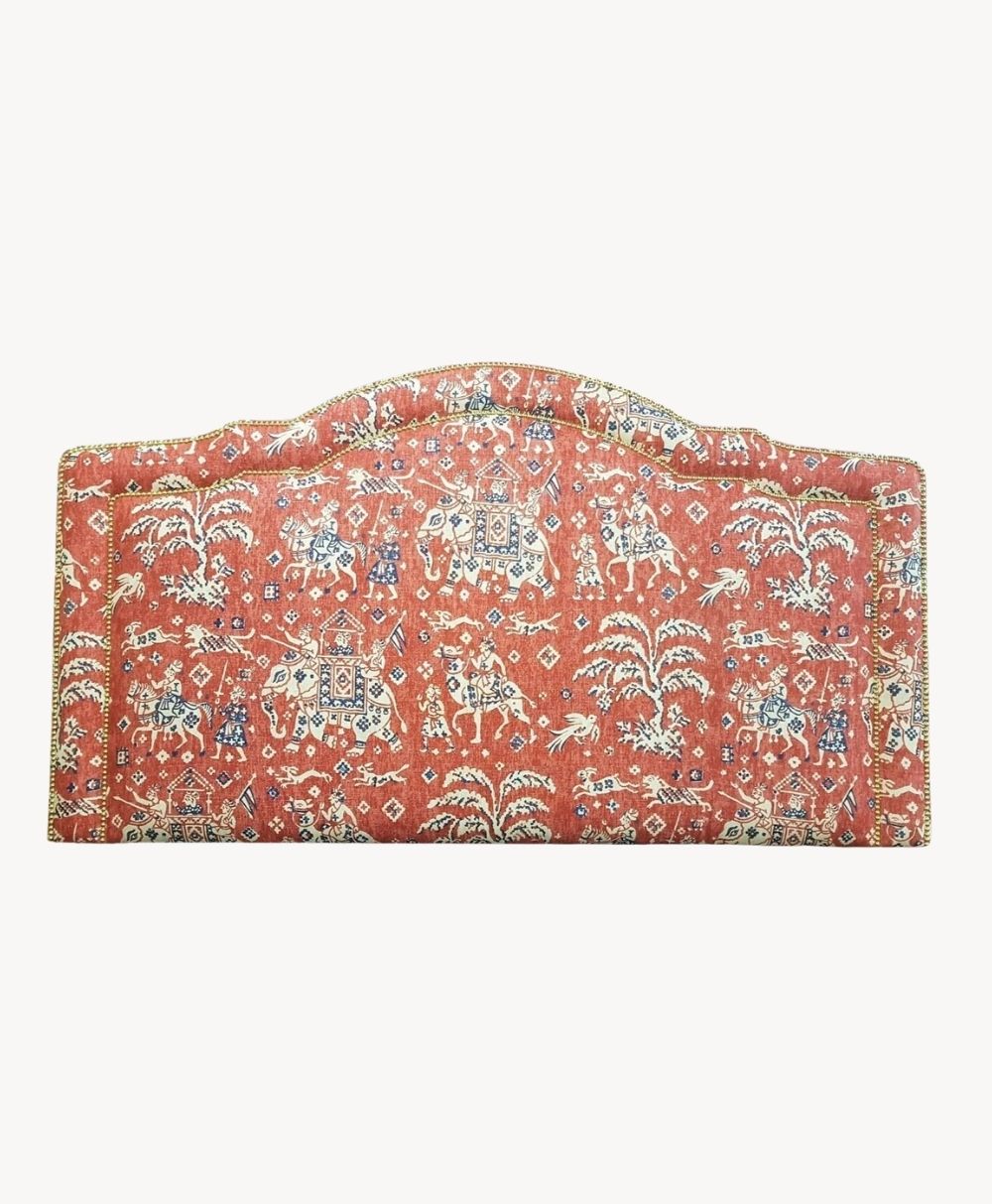 A decorative headboard upholstered in red fabric with intricate patterns featuring animals, trees, and geometric designs, bordered with a trim.