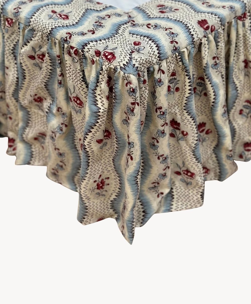 A ruffled tablecloth with a wavy zigzag pattern in blue, white, and beige, featuring red floral designs, draped over the corner of a table.