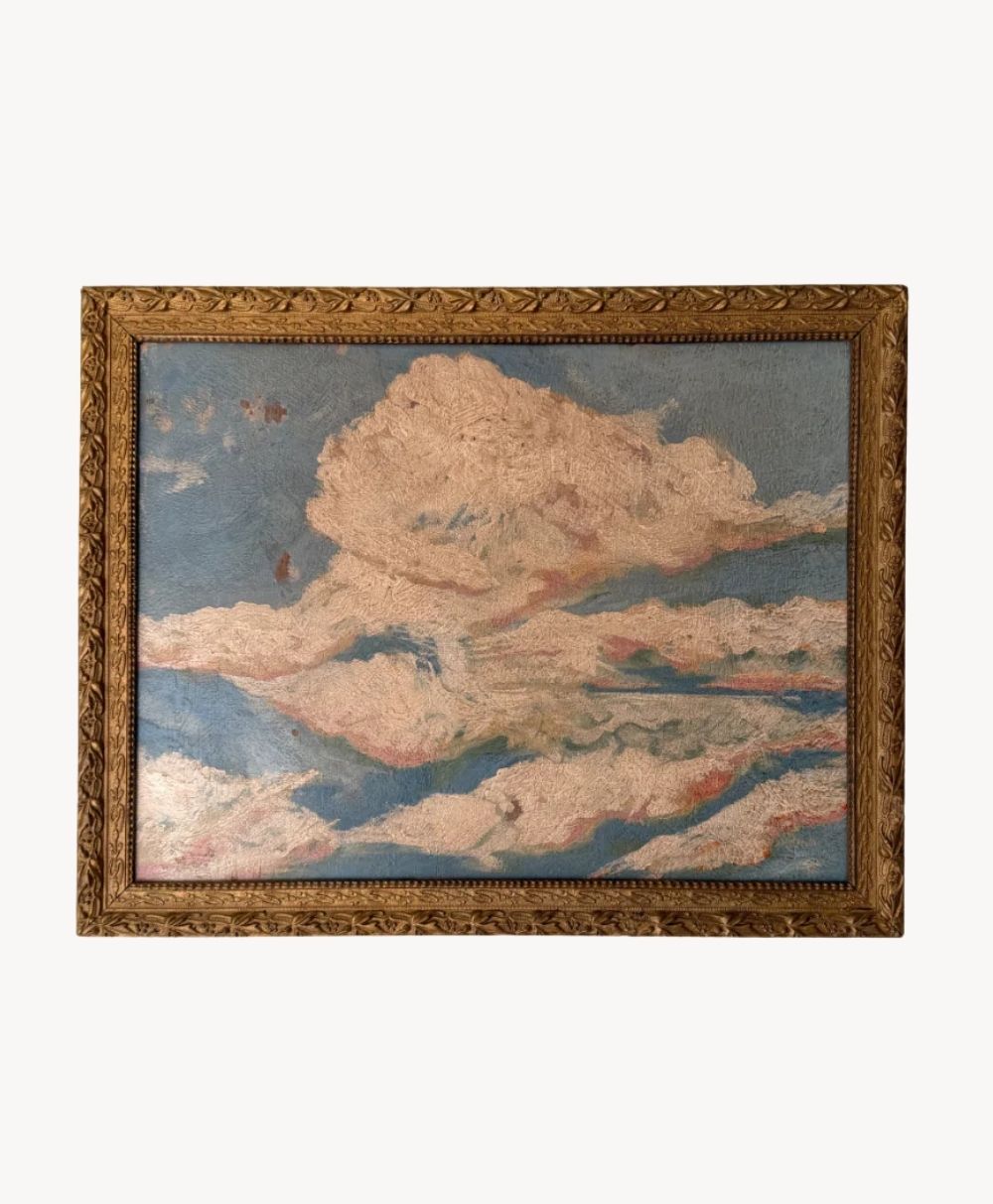 A framed painting depicts soft, pastel-colored clouds against a blue sky, with intricate gold detailing on the wooden frame surrounding the artwork.