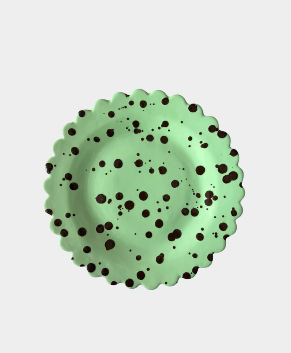 A round, light green plate with a scalloped edge and scattered dark brown spots, viewed from above on a plain white background.