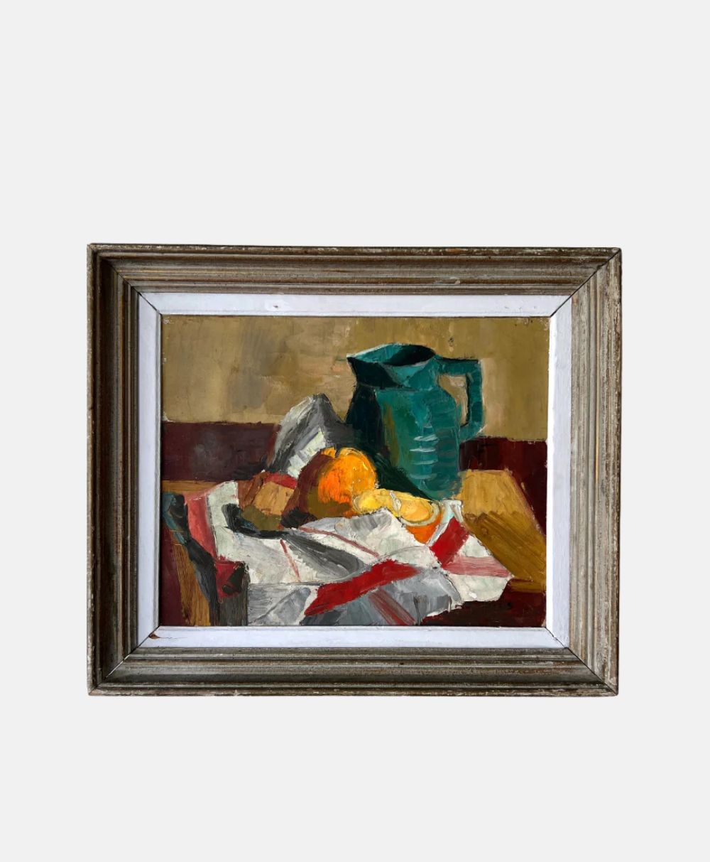 Framed still life painting of a teal pitcher, two oranges, and a folded striped cloth on a table, with earthy tones and geometric shapes dominating the composition.