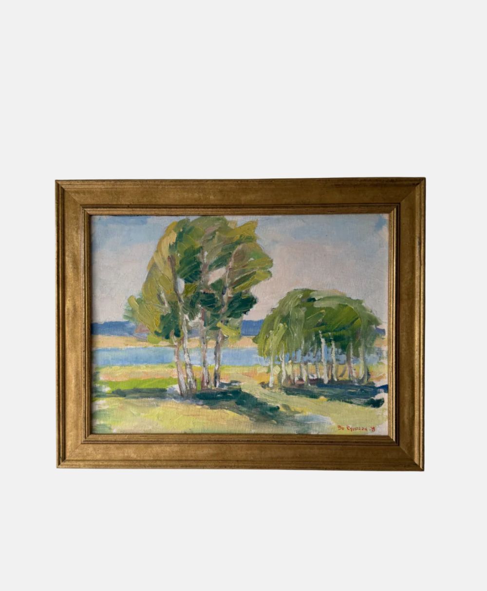 Framed painting of a summer landscape with green trees and grass near blue water, under a light blue sky with clouds. The frame is wooden with a golden-brown finish.