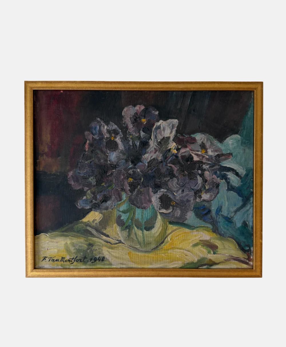 A framed painting of dark purple flowers in a glass vase on a yellow cloth, set against a dark background. The painting is signed “F. Van Montfort 1947” in the lower left corner.