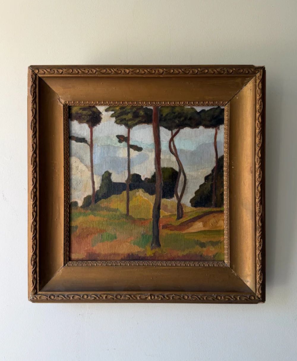 Framed painting of a landscape with tall, thin trees, grassy fields, and a distant view of bushes or forest under a partly cloudy sky. The frame is ornate and golden-brown.