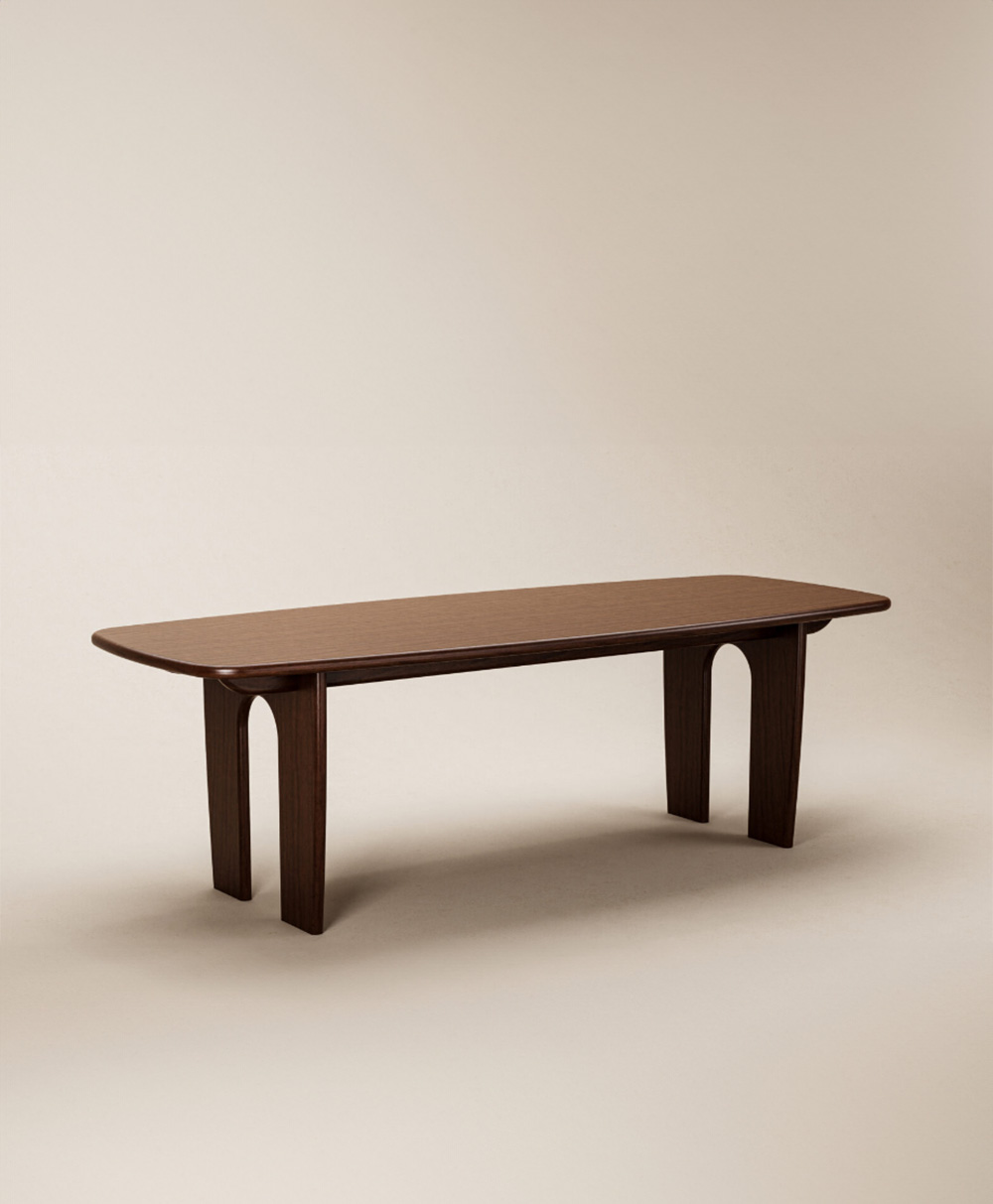 A minimalist wooden bench with a flat rectangular top, rounded edges, and four sturdy, arch-shaped legs, set against a plain beige background.