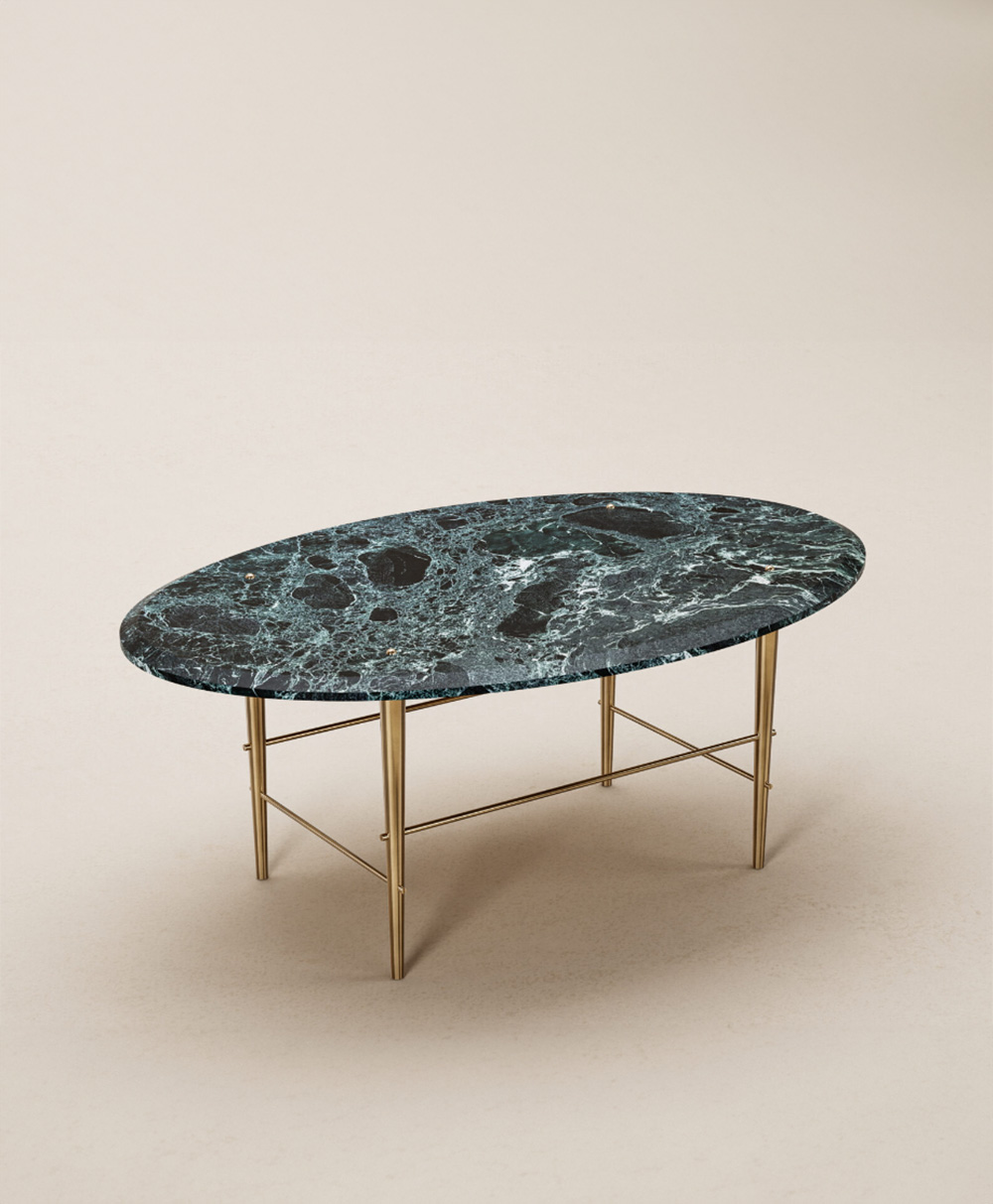 An oval-shaped coffee table with a dark green and black marble top and slender gold metal legs, placed on a light beige surface.