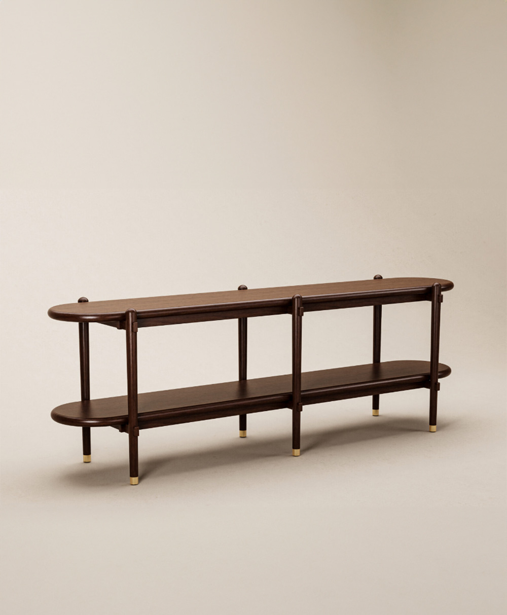 A long, dark wooden console table with rounded edges, two shelves, vertical supports, and small brass feet, set against a plain beige background.