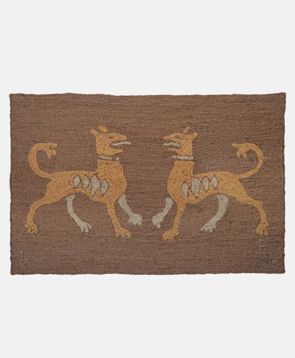 A brown woven textile featuring two stylized, yellow, dog-like creatures facing each other, each adorned with white shapes on their sides and a collar around their necks, set against a plain background.