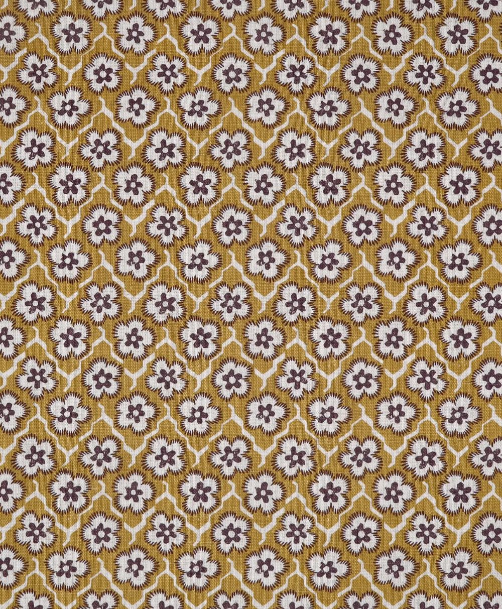 Repeating geometric floral pattern with white and brown flowers inside yellow diamond shapes, forming a symmetrical and intricate design on fabric or wallpaper.