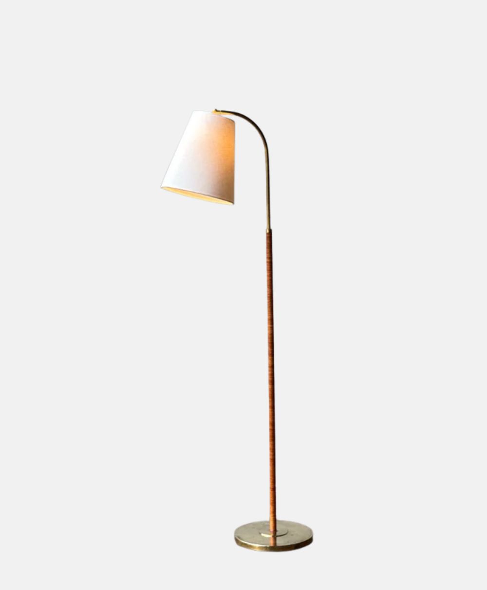 A modern floor lamp with a slender, brown wooden stand, a round metallic base, and a white, slightly tilted lampshade, set against a plain light gray background.