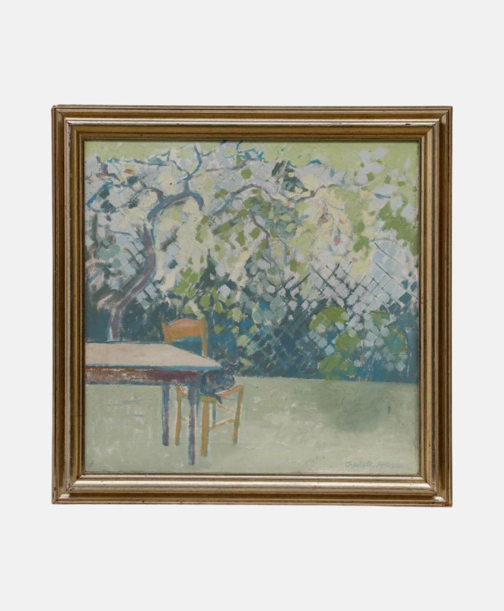 A framed painting depicts a garden scene with a leafy tree, a wooden table, and a single chair. The background features a fence, and the colors are soft greens, blues, and whites, creating a peaceful outdoor atmosphere.