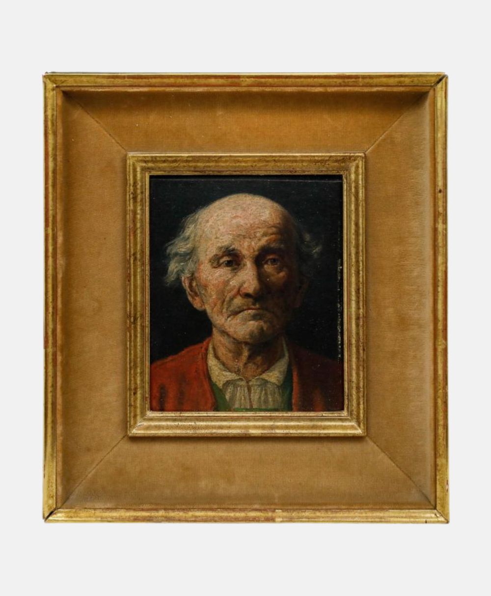 A framed oil painting of an elderly man with white hair and a somber expression, wearing a red garment over a shirt, set against a dark background, surrounded by a gold and tan frame.