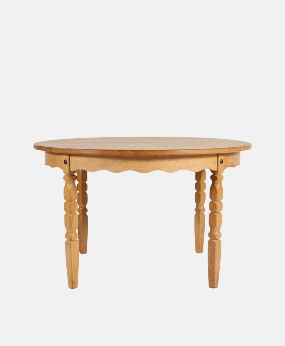 A round wooden table with four carved legs and a scalloped edge design, shown against a plain white background.