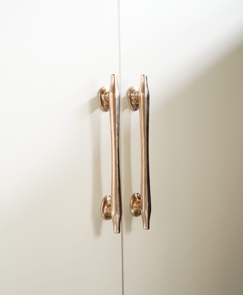 Two gold-colored metal handles are mounted vertically on white cabinet doors, positioned close to each other near the seam where the doors meet.