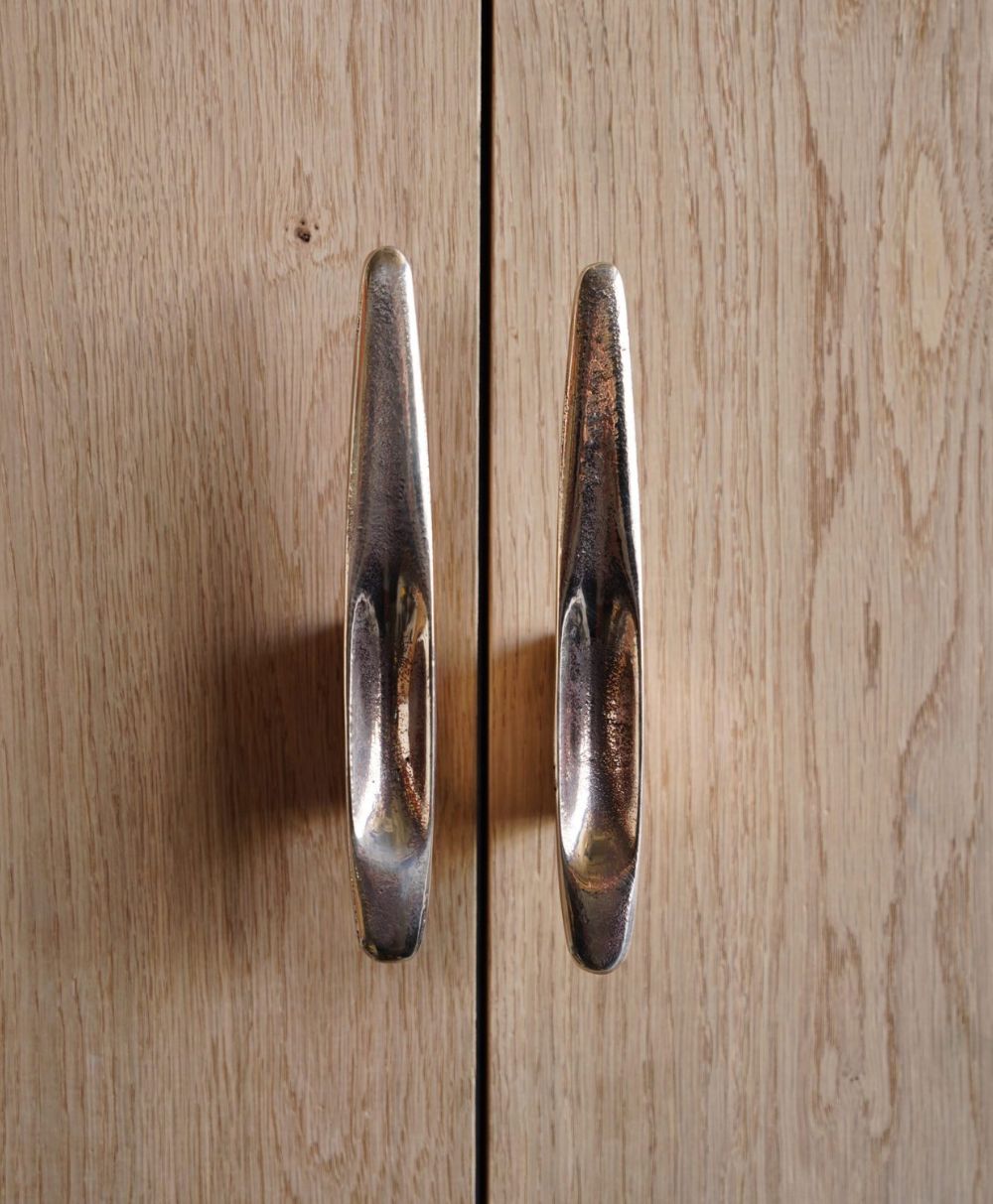 Two silver cabinet handles on light wood doors, positioned closely together and casting shadows, creating an abstract symmetrical pattern.