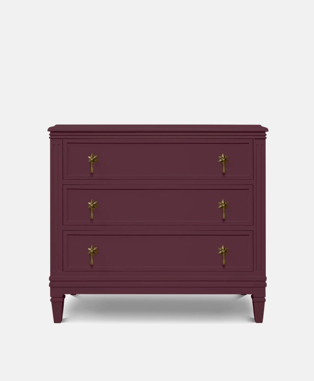 A maroon three-drawer dresser with gold star-shaped handles and tapered legs, set against a plain white background.