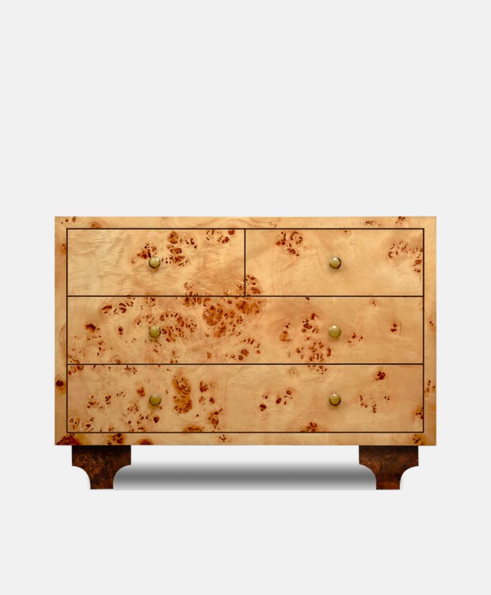 A wooden dresser with a light, natural finish and unique spotted wood grain, featuring four drawers with small round brass knobs and short, dark legs.