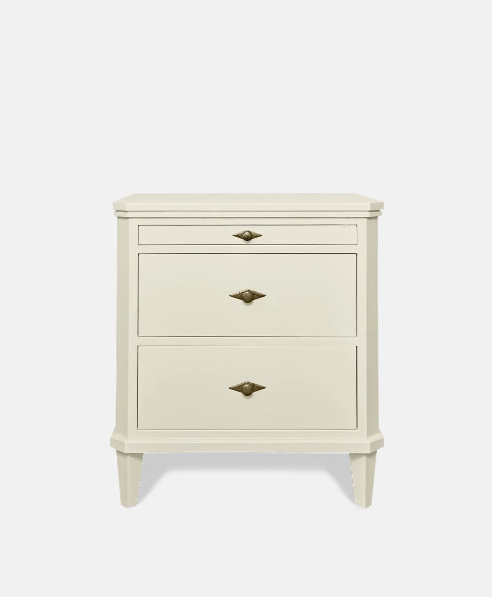 A cream-colored, three-drawer nightstand with gold handles and short, tapered legs, set against a plain white background.