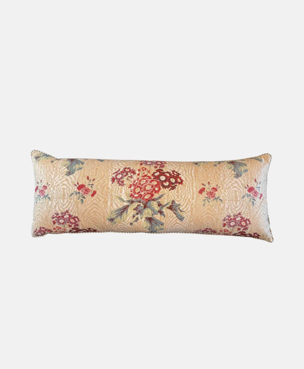A rectangular decorative pillow with a beige background, featuring a floral pattern in red, pink, and blue tones, and subtle wavy textured detailing.