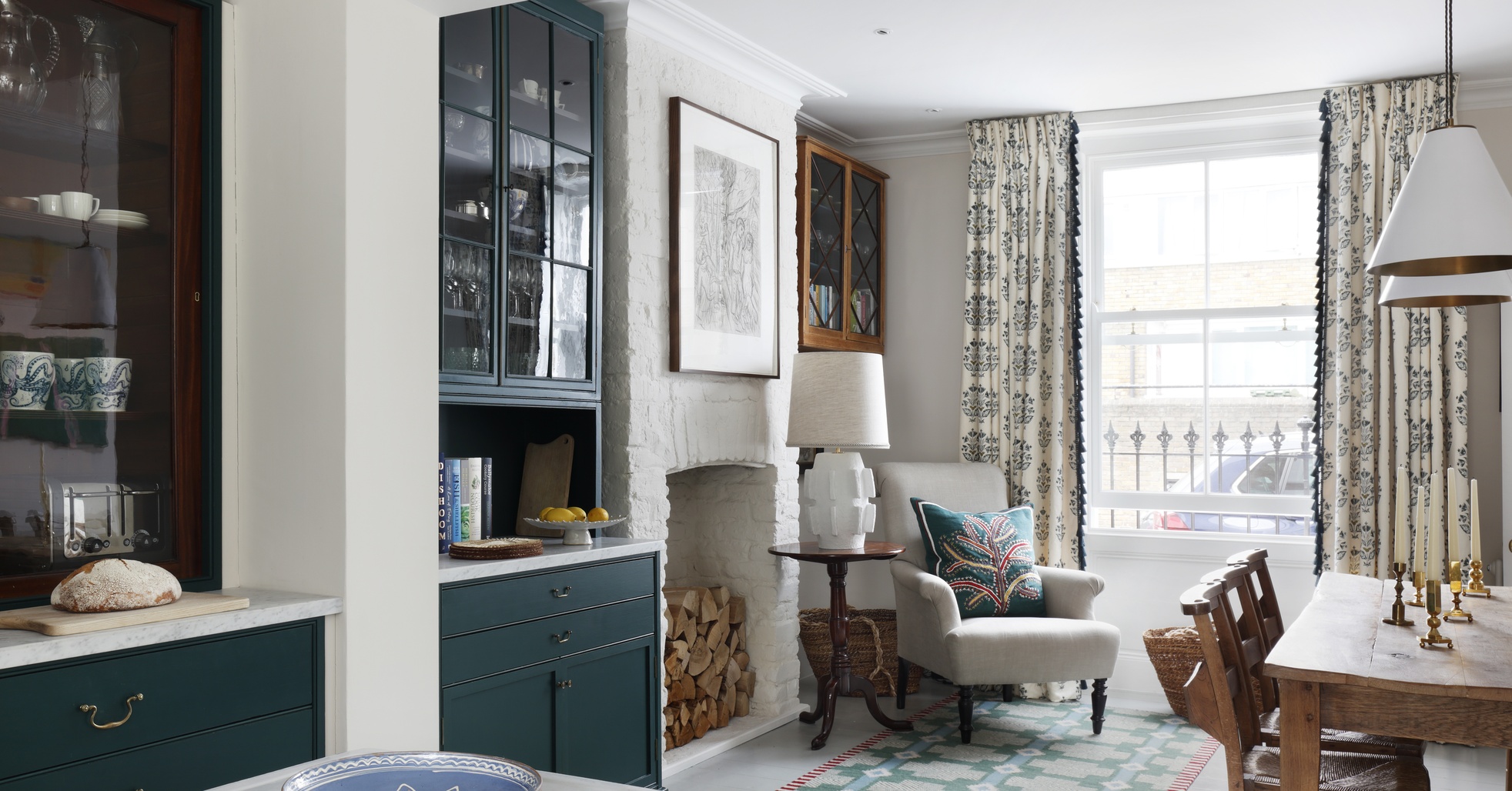 An English interior by Studio Peake: a Georgian cottage dining room with green glazed cabinets, a whitewashed brick fireplace and a rustic wooden table