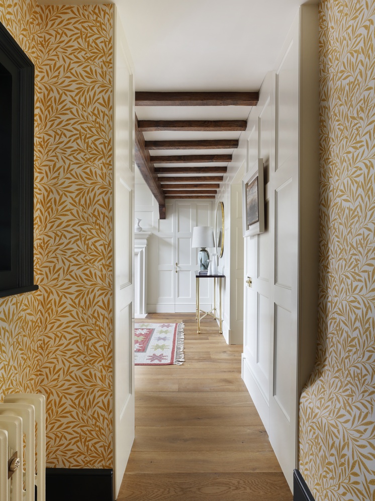 A hallway in an Arts and Crafts house restored by Studio Peake, with ochre willow-leaf wallpaper, panelled doors and exposed oak beams