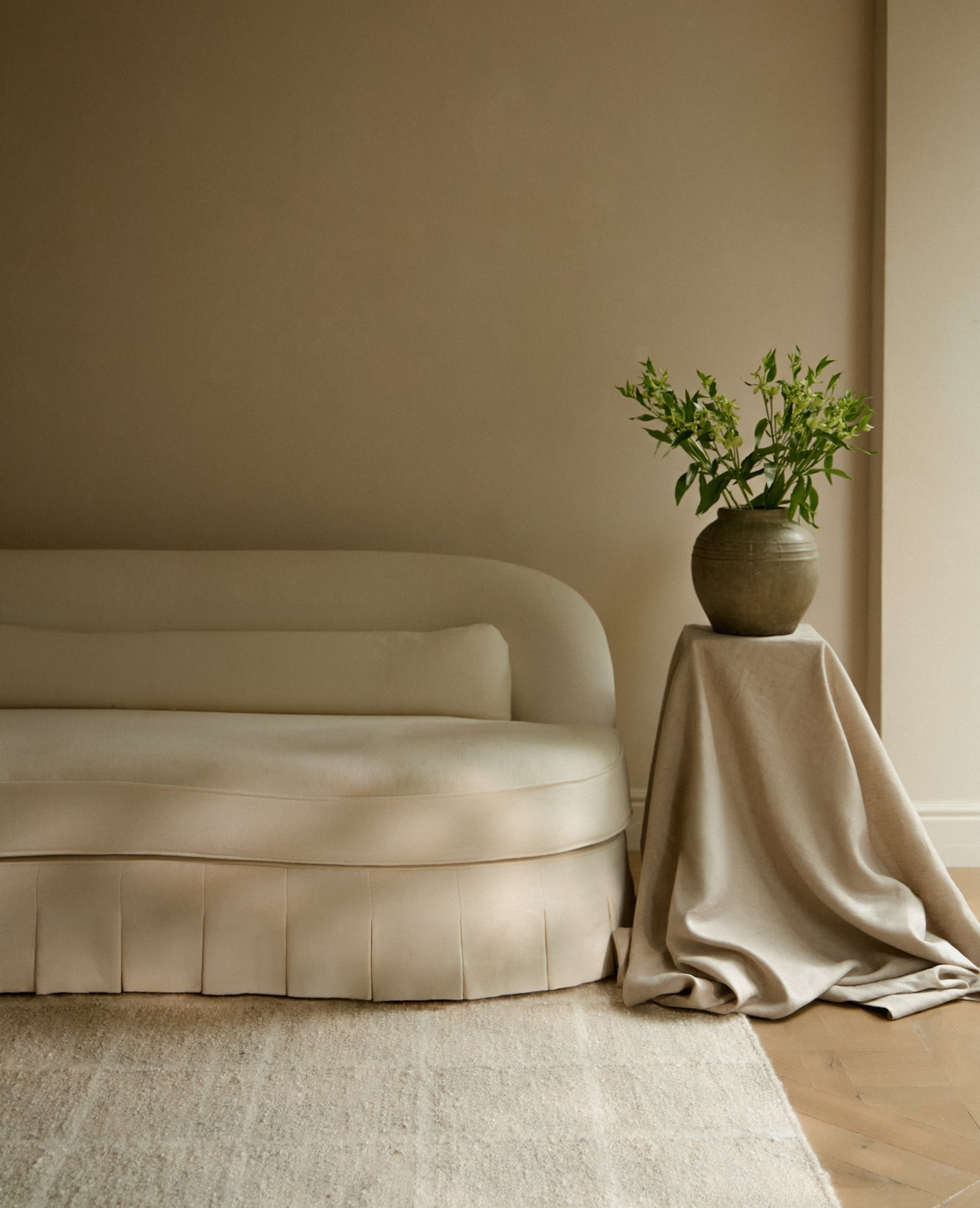 Coral & Hive Thula Frame rug in a softly neutral interior, featuring a sculptural cream Frances Jean sofa and a draped side table with a ceramic vase and greenery. Photography by Sarah Button. Scheme, UK